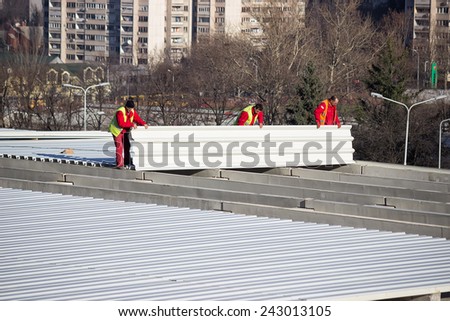 BELGRADE, SERBIA - DECEMBER 13: Roof sheet metal workers installing roof panels. Fastening metal roofing. Selective focus. At construction site in December 2014.