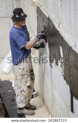 BELGRADE, SERBIA - MAY 24: Basement wall waterproofing,worker installing waterproofing tar sealer.Worker painting basement concrete wall with tar insulation material. At construction site in May 2014.