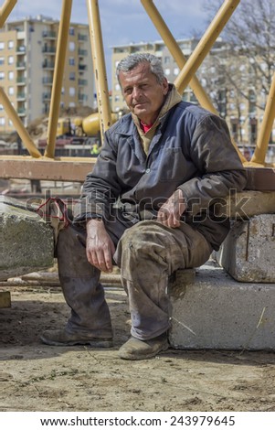 BELGRADE, SERBIA - MARCH 20: Senior builder worker resting after hard work in front of crane construction. At construction site in March 2014.