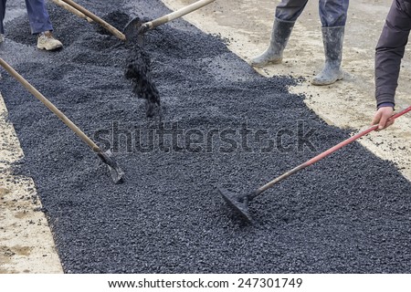 Road construction crew used shovels to scatter more asphalt over the top of the new pavement. At road construction site. Selective focus.