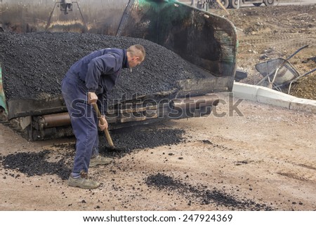 BELGRADE, SERBIA - JANUARY 21: Asphalt worker with a shovel in a front of a asphalt laying machine full of fresh asphalt. At road construction site in January 2015.
