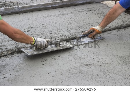 Leveling concrete with trowels, mason hands spreading poured concrete. Selective focus.