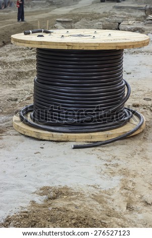 Roll of black industrial underground cable on large wooden reel at construction site. Four core al cable.  Selective focus and shallow dof.