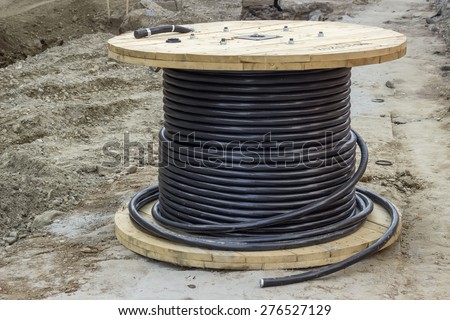 Roll of black industrial underground cable on large wooden reel at construction site. Four core al cable. Selective focus and shallow dof.