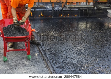 Crew placing mastic asphalt road and pea gravel surfacing, laying of mastic surface. Selective focus and shallow dof.