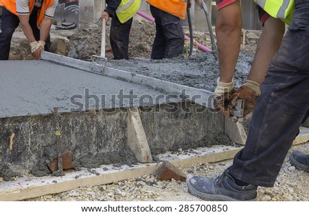 Leveling wet concrete with a metal screed. Worker hands using a screed board to level the surface. Selective focus and shallow dof