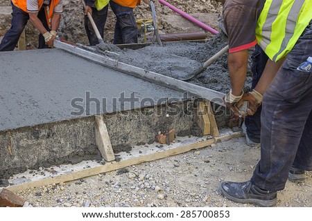 Leveling wet concrete with a metal screed. Worker hands using a screed board to level the surface. Selective focus and shallow dof.