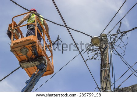 Utility pole worker installs new cables on an electric pole from lift bucket.