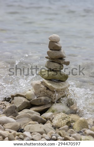 Pile of stones in the balance on sea coast with sea wave in the background. Concept of stability, balance and harmony.