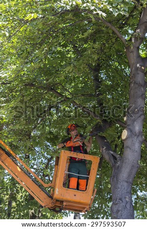 BEOGRAD, SERBIA - JULY 16, 2015: Worker in bucket with a chainsaw trims trees. Worker using chainsaw from hydraulic mobile platform for dead wooding tree trimming.