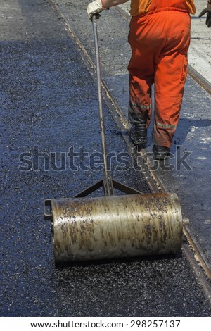 Worker using a hand roller for mastic asphalt paving. Selective focus and shallow dof, some motion blur present.