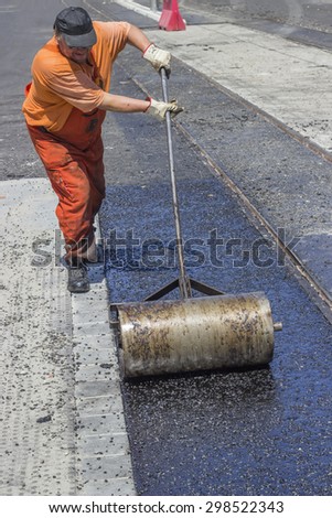 BEOGRAD, SERBIA - JULY 16, 2015: Worker using a hand roller for mastic asphalt paving. Selective focus and shallow dof, some motion blur present.