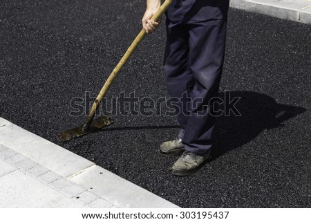 Worker using asphalt lute to level the asphalt and prepare it for compaction. Selective focus and some motion blur present.