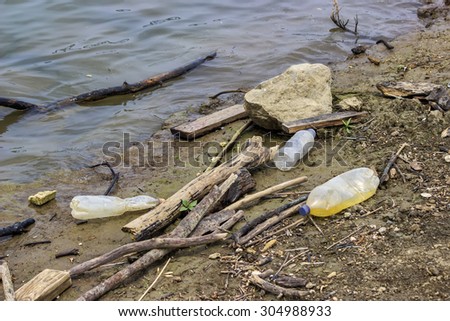 Plastic bottles and garbage waste on the shore of a river. Selective focus.