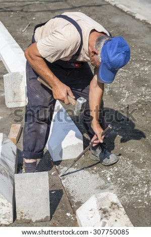 BEOGRAD, SERBIA - JULY 30, 2015: Worker using chisel and hammer for paving work. Selective focus and shallow dof.