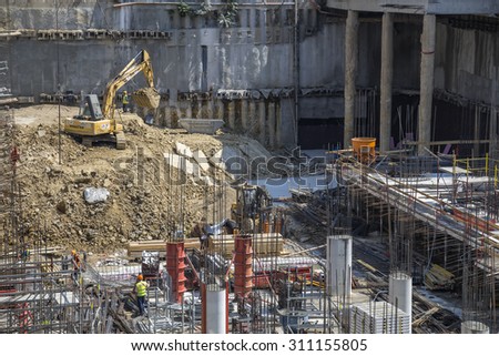 BEOGRAD, SERBIA - AUGUST 15, 2015: Excavating machine in the pit digging deep on building site with workers making reinforcement metal for concrete pouring. Made with shallow depth of field.