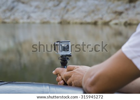 Hand holding small action camera with waterproof case and shooting from a boat on the river. Made with shallow depth of field.