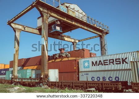 BELGRADE, SERBIA - OCTOBER 28, 2015: Old and rusty portal crane lifting container from train trailer. Containers and container handling, rail mounted crane. Made with vintage style.