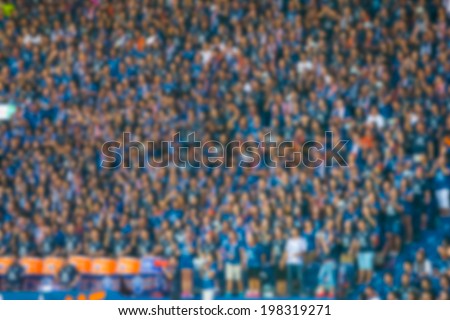Blurred crowd of spectators on a stadium with a football match.