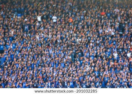 Blurred crowd of spectators on a stadium with a football match.