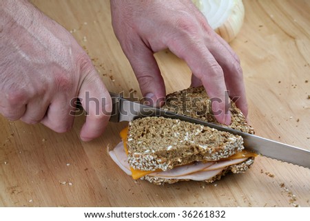 Hands cutting turkey sandwich on counter top.