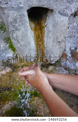 hands washing under stone water source
