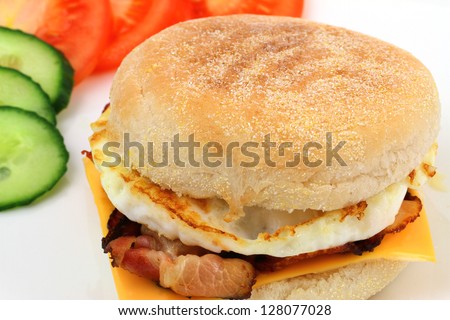 English muffin with fried egg, bacon, Cheddar cheese, tomato and cucumber