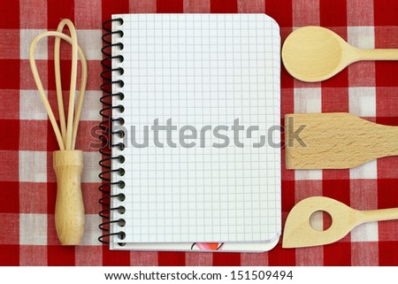 Notebook and wooden cooking utensils on red and white checkered tablecloth