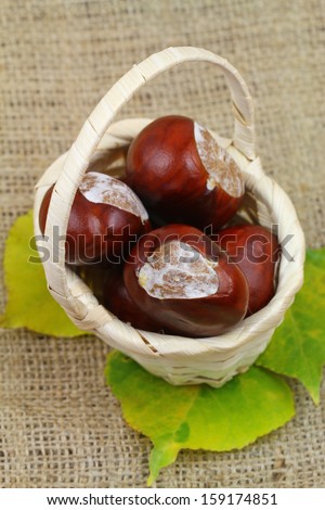 Chestnuts in miniature wicker basket on jute surface