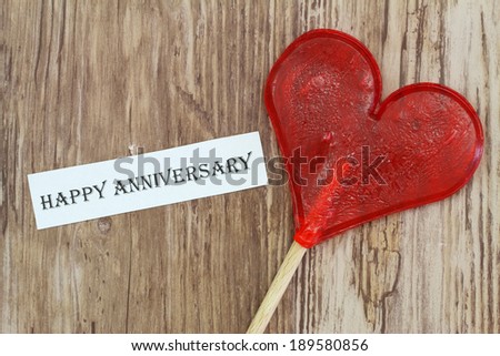 Happy Anniversary card with heart shaped lollipop on wooden surface