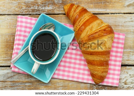 Butter croissant and black coffee on pink checkered cloth on rustic wooden surface