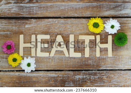 Health written with wooden letters on rustic surface with santini flowers