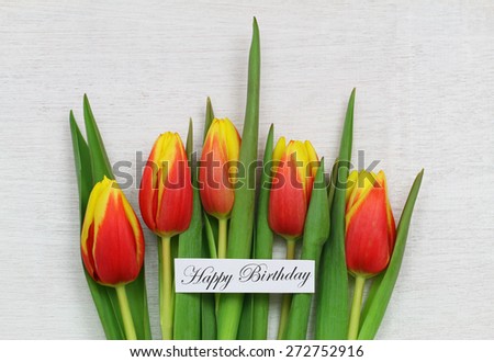 Happy birthday card with red and yellow tulips on white wooden surface