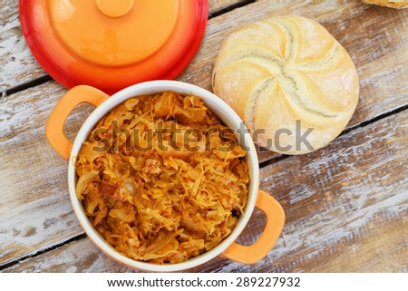 Polish bigos in saucepan and bread roll on rustic wooden surface