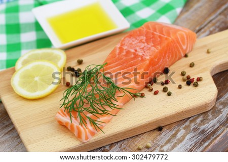 Raw salmon steak on wooden board with lemon, pepper and olive oil