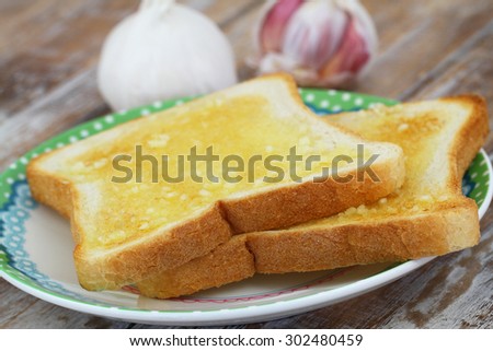 Slices of garlic bread on plate on rustic wooden surface