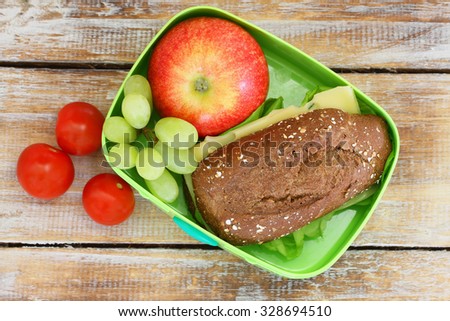 Healthy school lunch box with brown bread cheese sandwich, red apple, grapes and cherry tomatoes