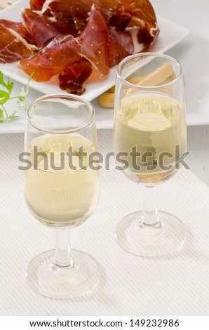 Spanish cuisine. Tapas. Two glasses of Sherry Wine. Sliced Serrano Ham in the background. Selective Focus. Vino de Jerez.