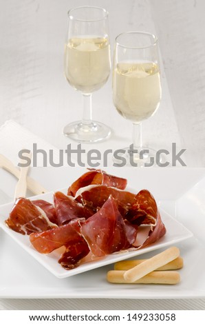 Spanish cuisine. Tapas. Sliced Serrano Ham in a white plate.Two glasses of Sherry Wine in the background. Selective Focus. Jamon Serrano.