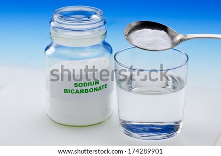Sodium bicarbonate pouring in a glass of water. Blue background.