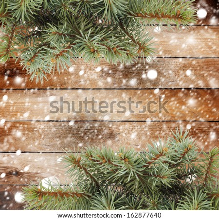 Christmas tree branch on the snow-covered wooden background
