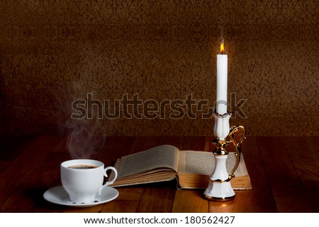 Hot cup of fresh coffee on the wooden table with  candle and book