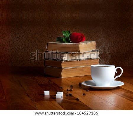 Hot cup of fresh coffee on the wooden table and stack of books to read with red rose