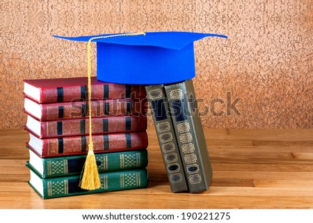 Graduation mortarboard on top of stack of books on wooden background of wall