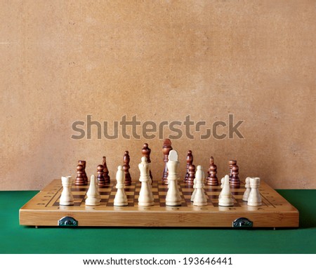 Wooden chess board with figures on green table and old wall