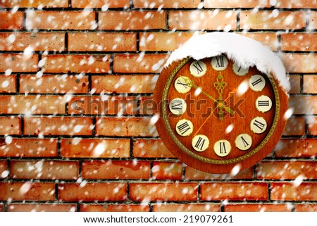Snow-covered clock on background of old brick wall