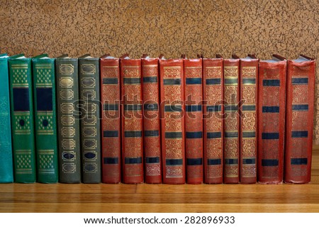 Richly decorated volumes of books with a gold lettering on the beautiful wooden shelf