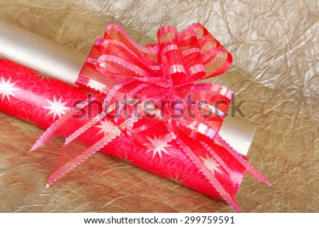 Rolls of multicolored wrapping paper with red bow for gifts on gold abstract background. View from above with copy space
