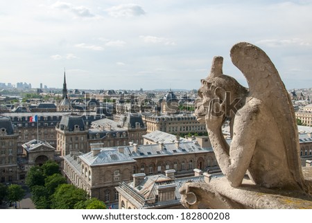 A bored gargoyle sits on top of Notre Dame surveying the Parisian cityscape below.