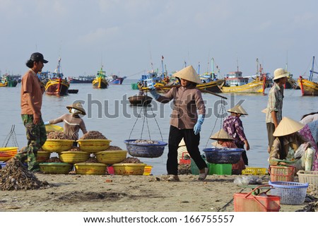 MUI NE,VIETNAM - APRIL 7, 2010 : An unidentified woman uses a carrying pole to transfer baskets of fish along the beach, on April 7, 2010, in Mui Ne, Vietnam.